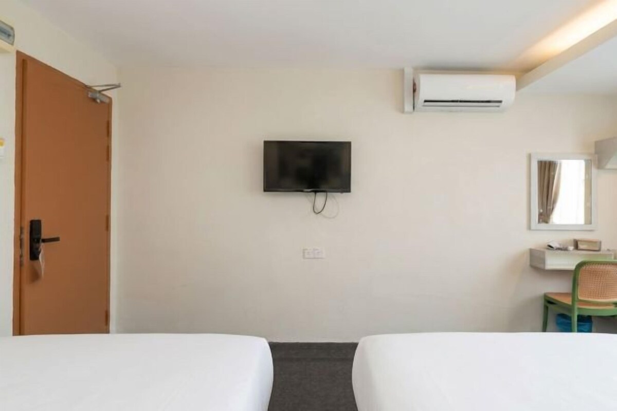 Habitación de hotel con dos camas, un televisor, un equipo de aire acondicionado, un escritorio pequeño con una silla y un espejo.