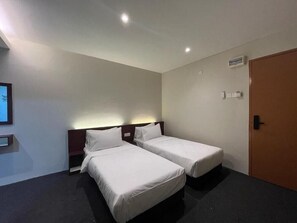 A hotel room with two single beds, a wooden headboard, a small bedside table, a wall-mounted light, and a door. - Swing and Pillows @ Malacca Mahkota Parade (Melaka)