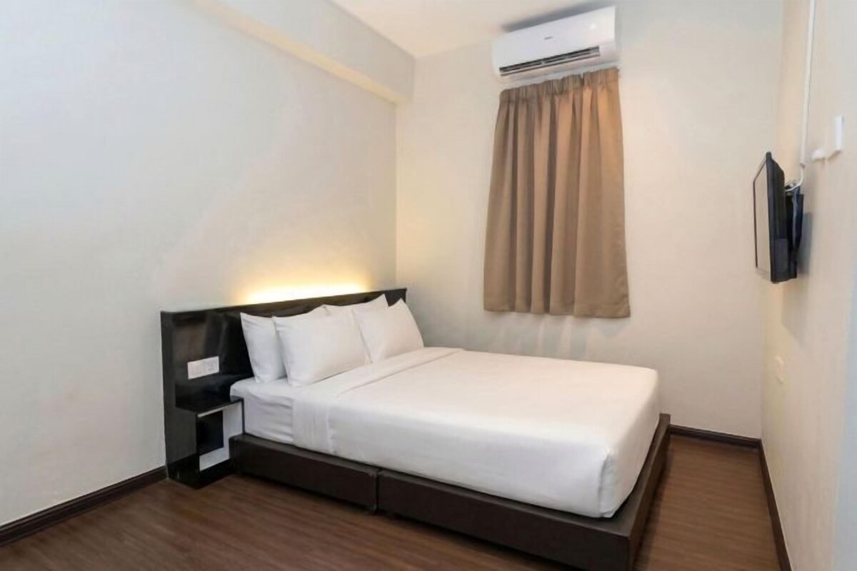 A hotel room with a bed, bedside table, and a mounted TV.