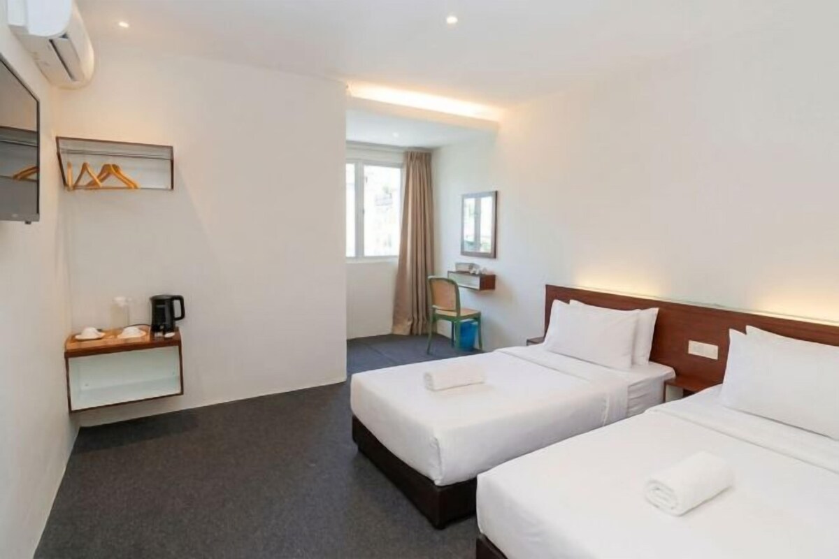 A hotel room with two beds, a desk with a chair, a coat rack, and a bathroom visible through an open door.