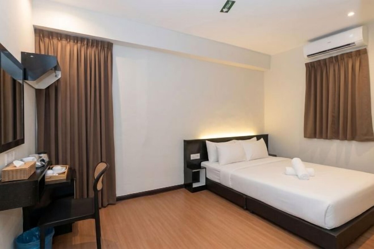 A hotel room with a bed, a desk with a chair, a small table, and an air conditioning unit.