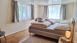 Une chambre à coucher avec un lit, une chaise, une table de chevet avec une lampe et une fenêtre avec des rideaux.