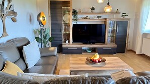 Un salon moderne avec un canapé en cuir, une table basse en bois ornée de fruits, un téléviseur et des objets décoratifs.