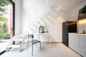 A modern kitchen with a built-in refrigerator, a dining area with a chair and table, and a staircase with a geometric design. - Express by M Village 59 Thao Dien, a brand of Modern Village Lifestyle (Ho Chi Minh City)
