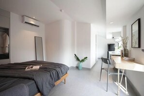 A modern bedroom with a bed, a desk, and a chair. There is a plant and a mirror on the wall. - Express by M Village 59 Thao Dien, a brand of Modern Village Lifestyle (Ho Chi Minh City)