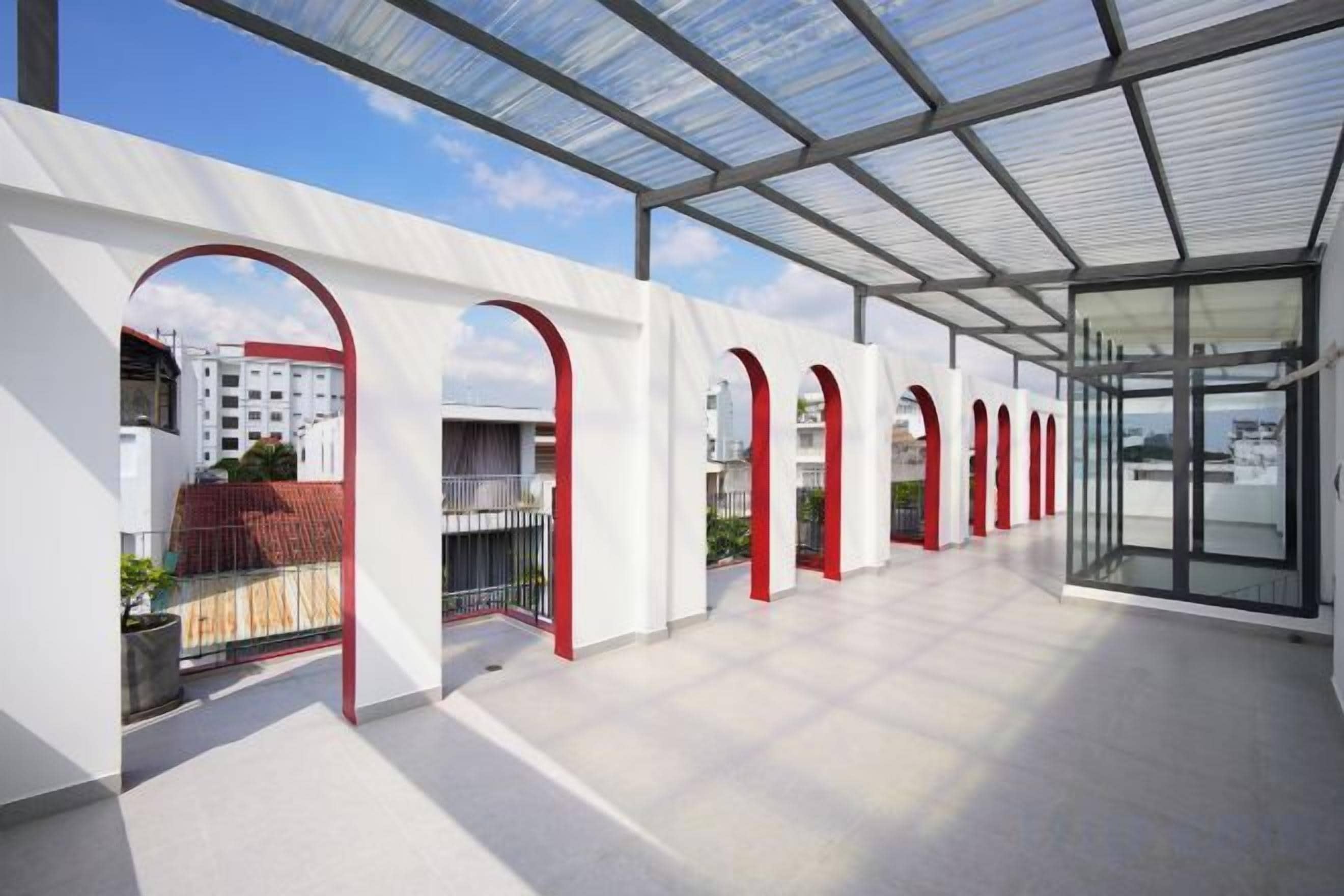 A covered outdoor area with a glass roof, white walls, and red arches.