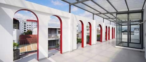 A covered outdoor area with a glass roof, white walls, and red arches.