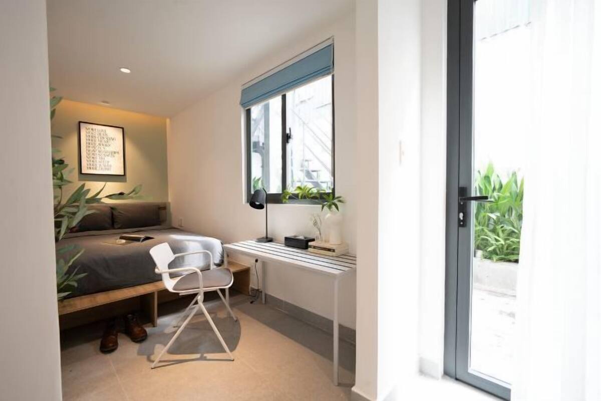 A compact bedroom with a bed, a desk, and a chair, featuring a window with a view of greenery outside.
