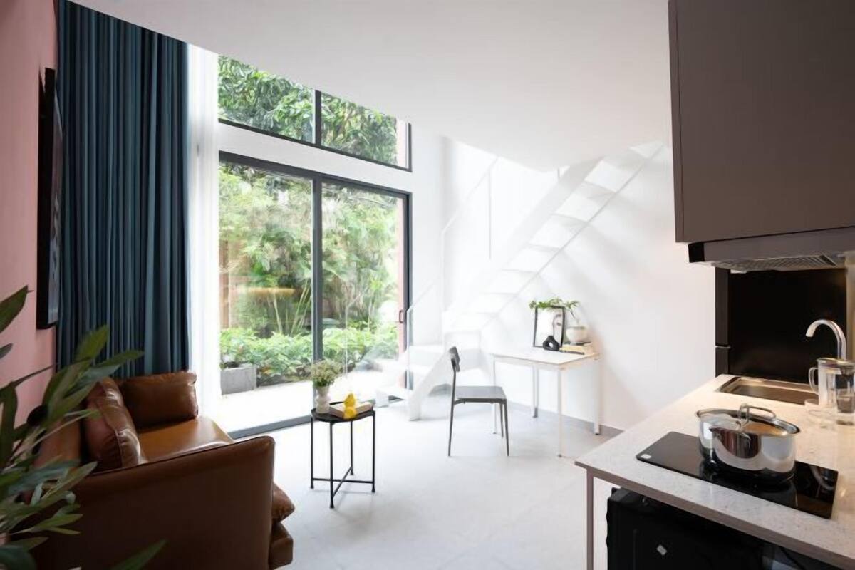 A modern kitchen with a dining area, large windows, and a view of greenery.