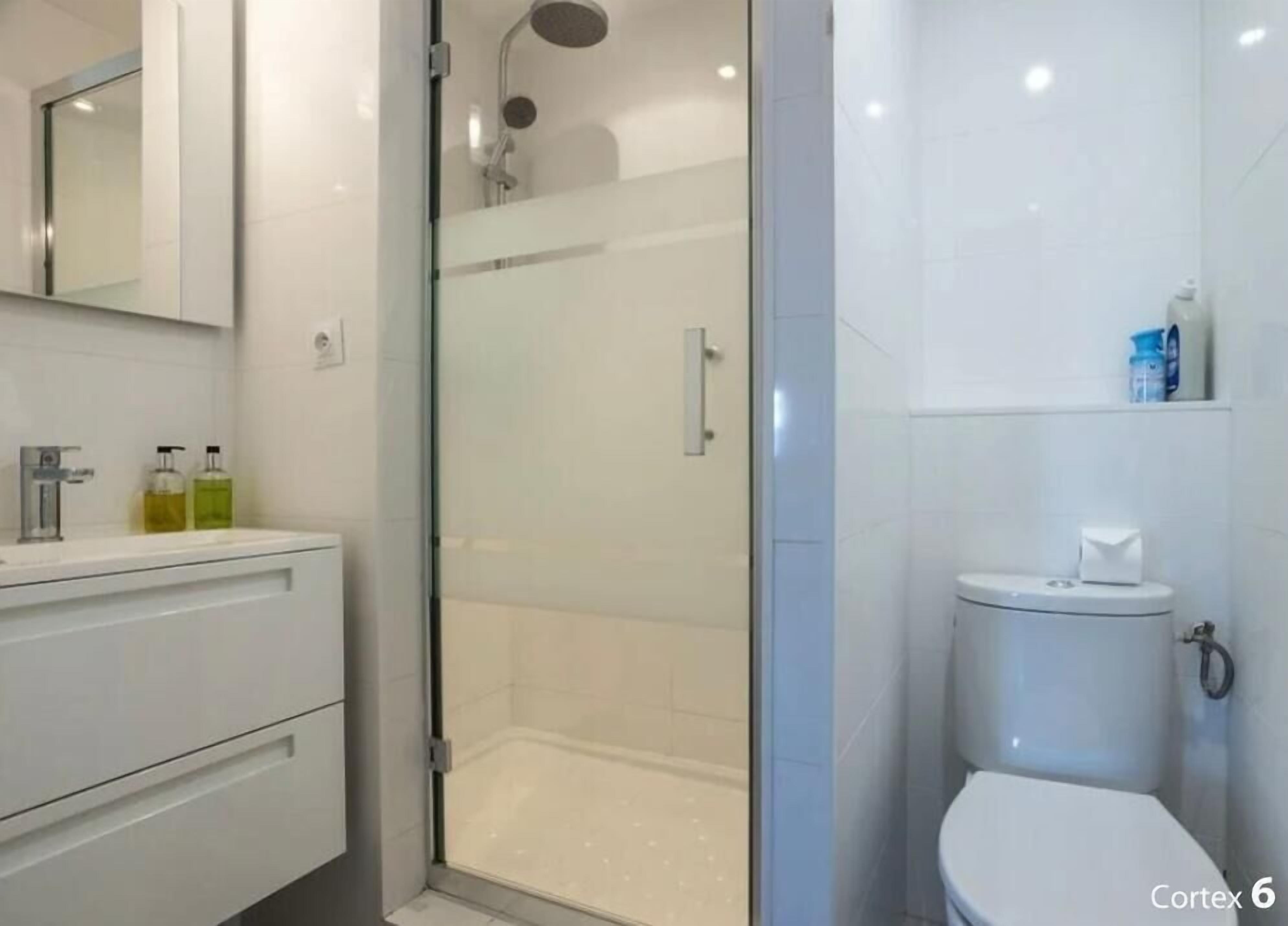 A modern bathroom with a glass-enclosed shower, a white toilet, and a vanity with a mirror and toiletries.