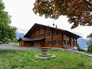 A wooden chalet with a sloped roof, multiple windows, and a stone fountain in the foreground. - Wonderful private villa for 10 guests with terrace and panoramic view (Ollon)