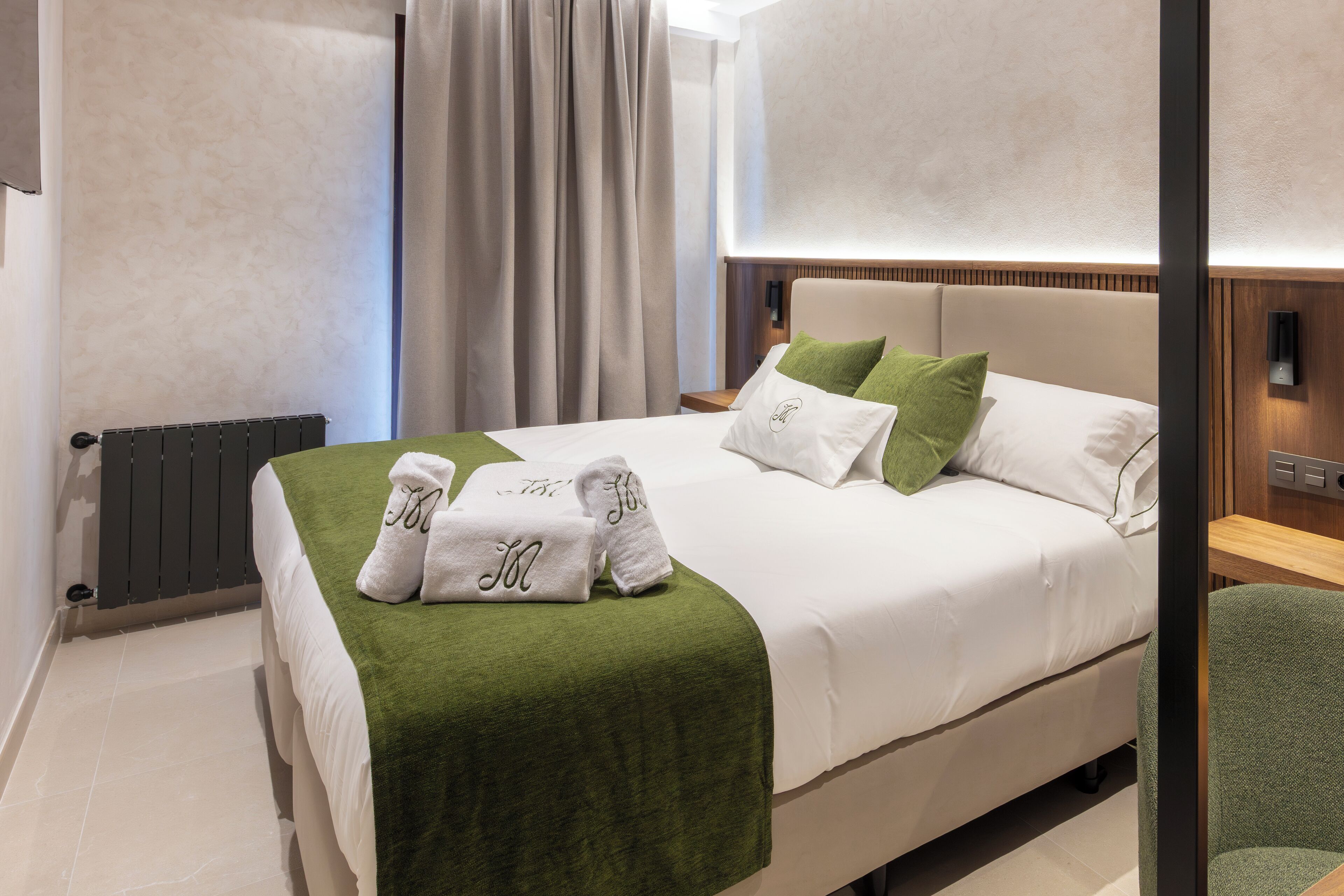 Una cama bien hecha con un edredón verde, sábanas blancas y dos almohadas verdes.