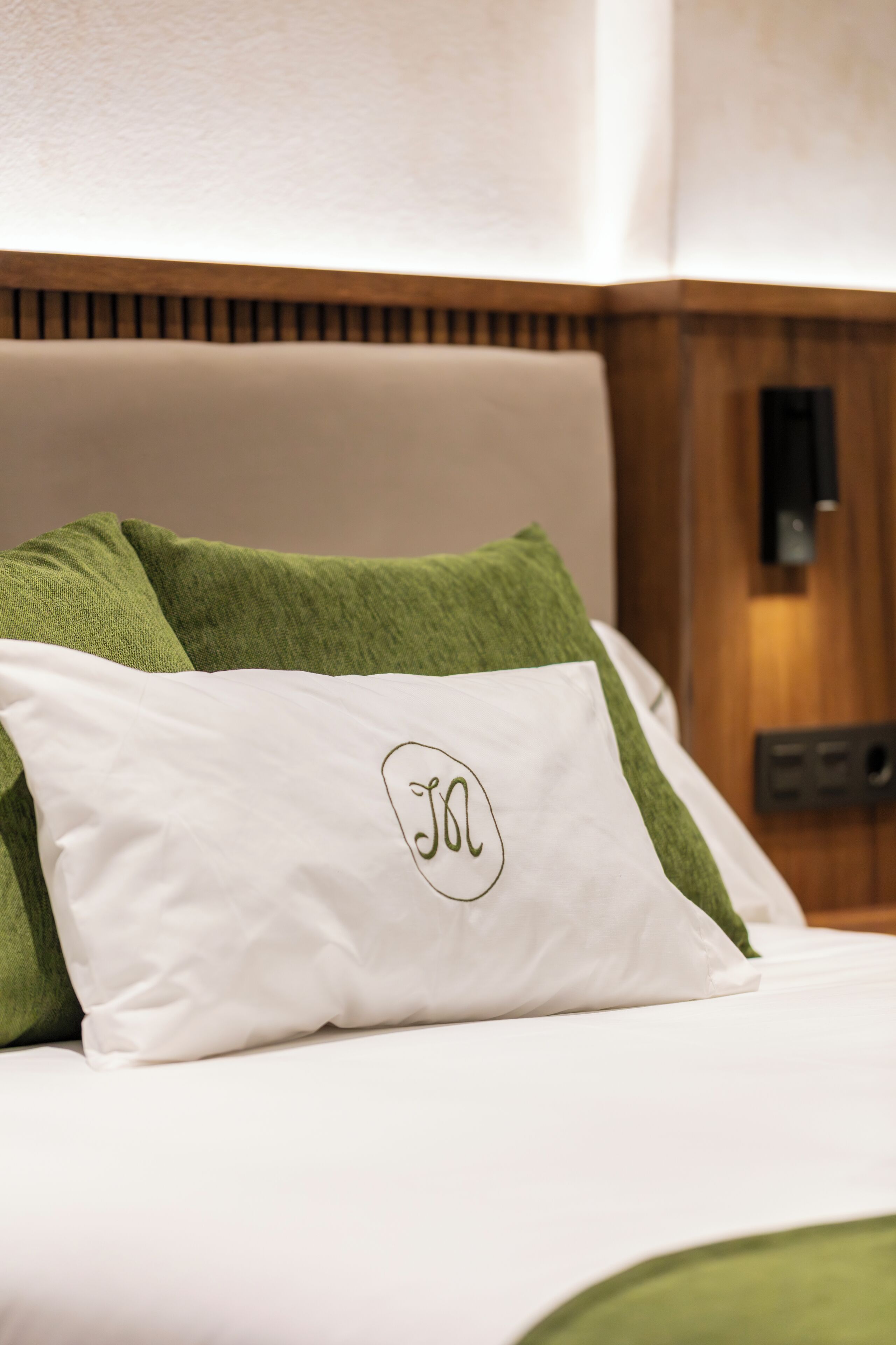 A neatly made bed with green and white pillows, one of which has a monogram.