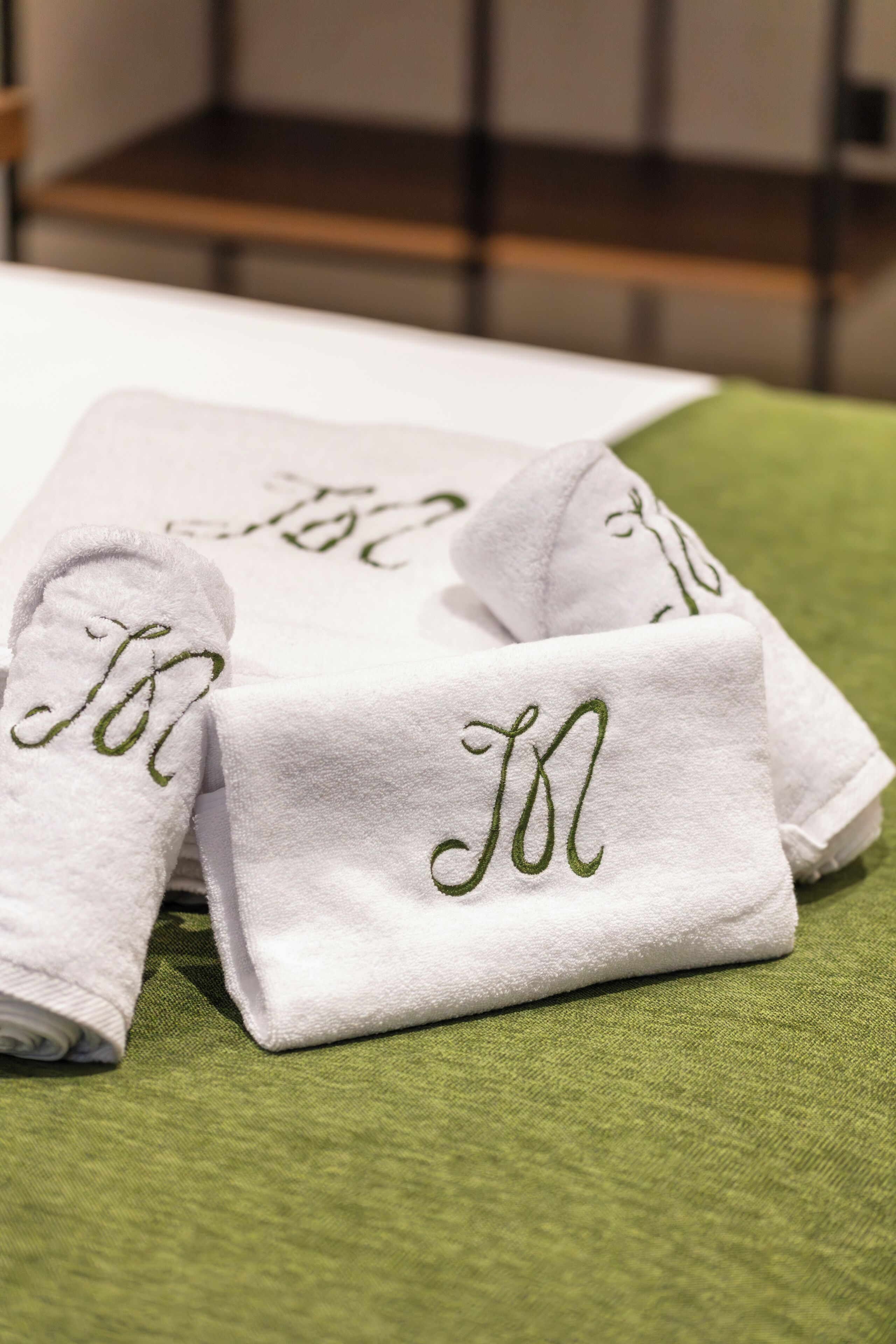 Toallas blancas dobladas con cuidado y con iniciales bordadas sobre una superficie verde con textura.