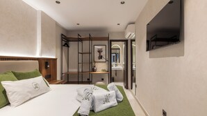 Ein modernes Hotelzimmer mit einem Bett, grünen Handtüchern, einem Fernseher und einem durchgegangenen Tür sichtbar erkennbaren Badezimmer.