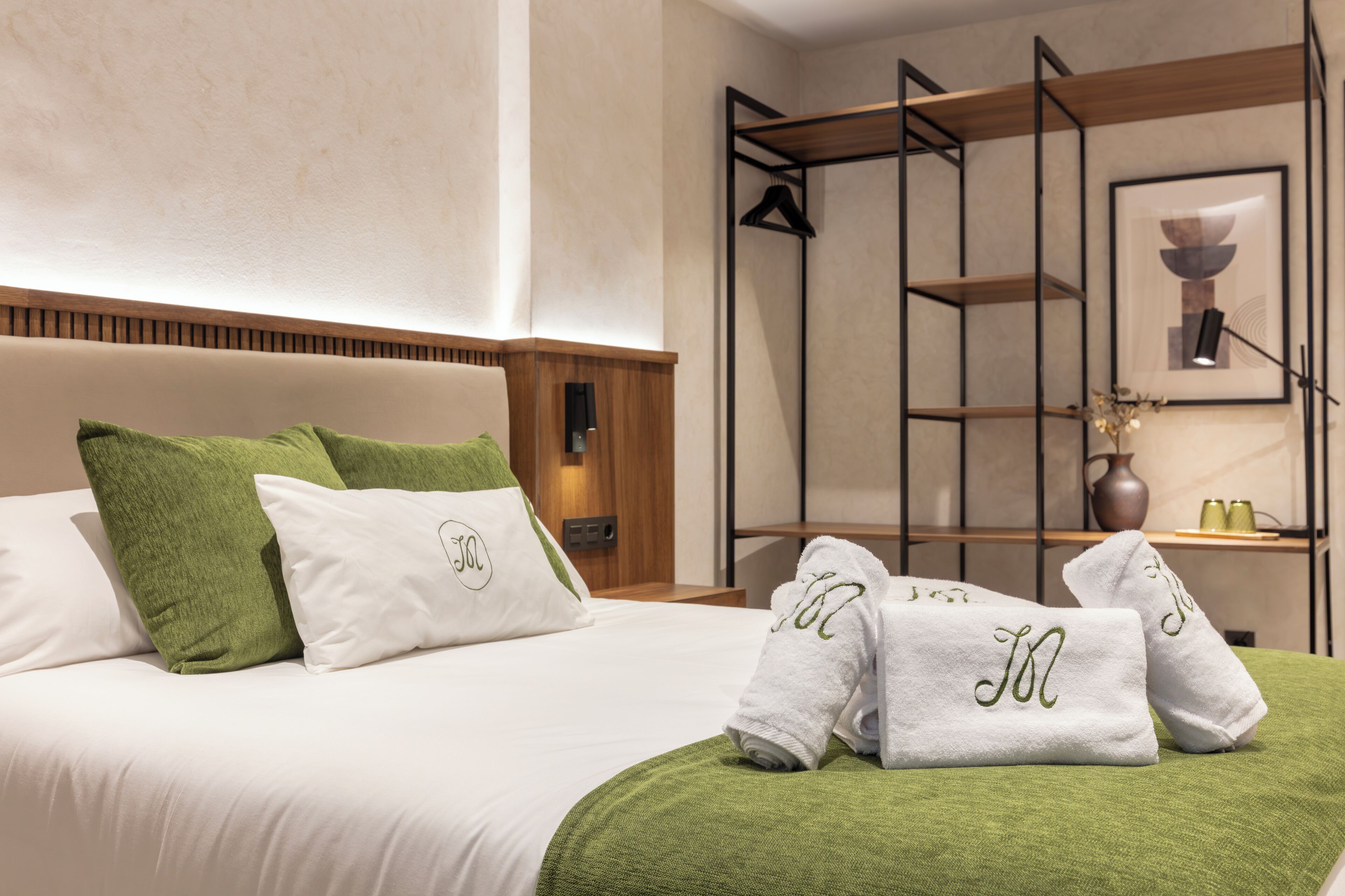 A hotel room with a bed, green and white pillows, a green throw blanket, and towels with monogrammed initials.