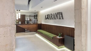 Ein Empfangsbereich mit einem hölzernen Empfangstresen, einer gepolsterten grünen Bank und einem an der Wand befestigten Schild mit der Aufschrift 'A. GARANTIA'.