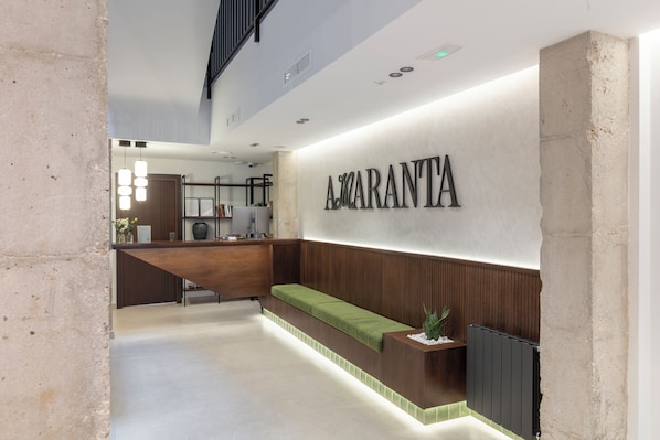 A reception area with a wooden reception desk, a green cushioned bench, and a wall-mounted sign reading "A. GARANTIA". - Amaranta Hotel Boutique (Ronda)