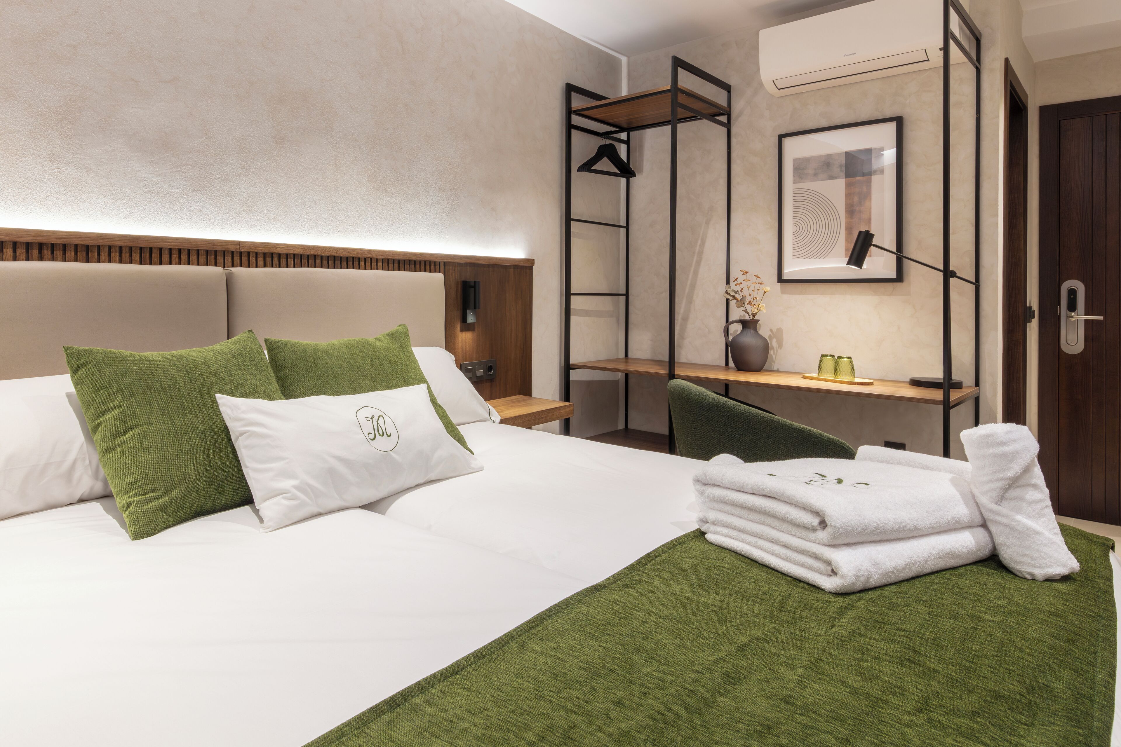 A modern hotel room with a bed, green pillows, a desk, and a bathroom.