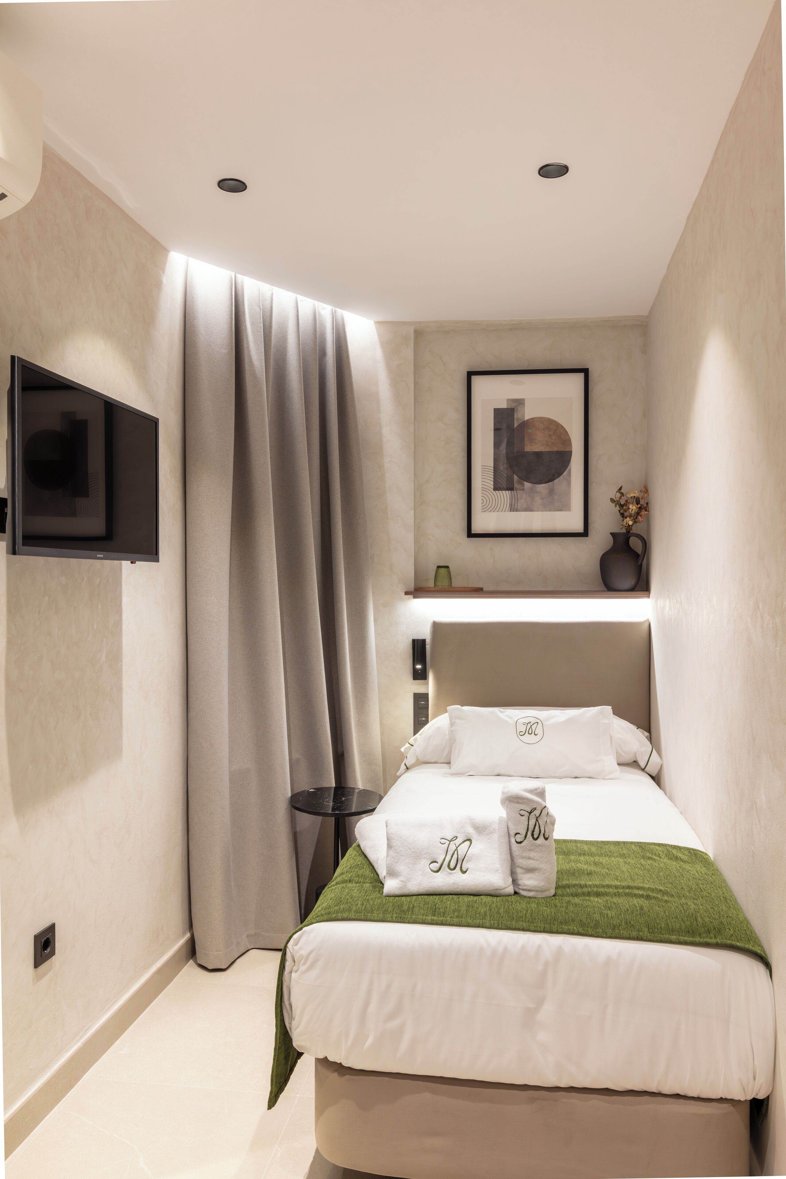 A modern bedroom with a bed, a mounted TV, a painting, and a vase on a shelf.
