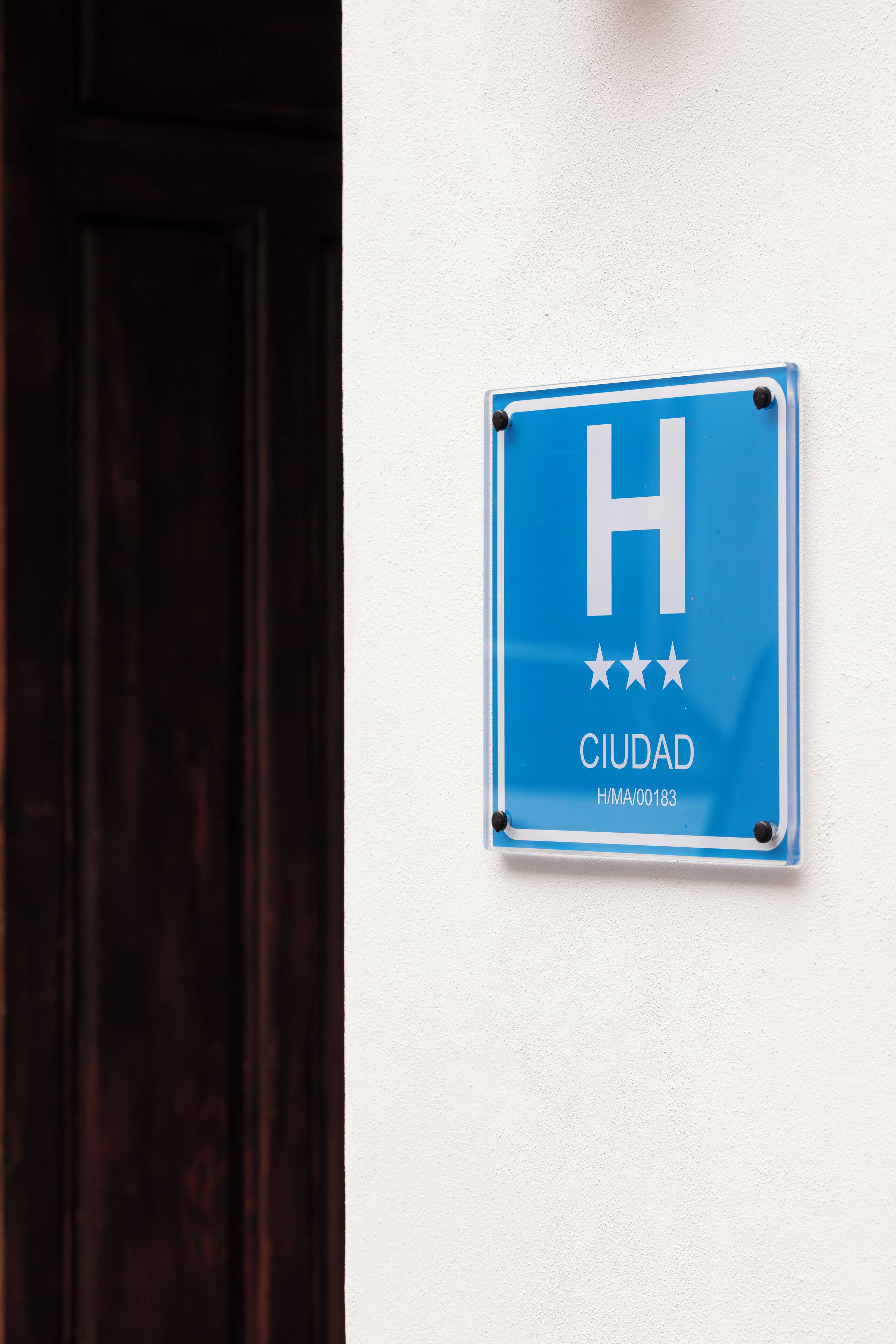 A blue sign with a white 'H' and three stars, labeled 'CIUDAD' and a code 'H/M/00183'.