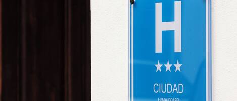 A blue sign with a white 'H' and three stars, labeled 'CIUDAD' and a code 'H/M/00183'.