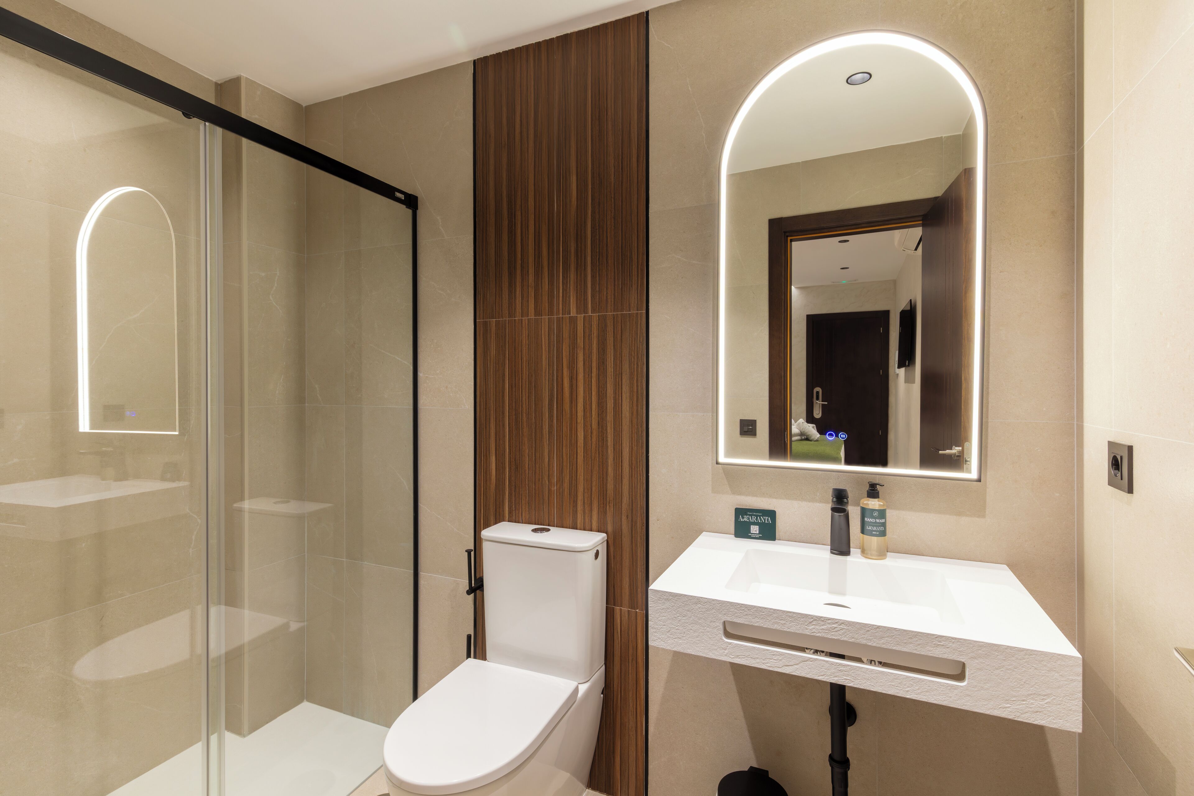 A modern bathroom with a glass shower enclosure, a white toilet, and a sink with a mirror above it.
