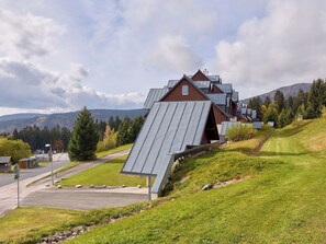Een modern gebouw met een schuin dak en een opvallende schoorsteen, omgeven door een gazon en bomen.