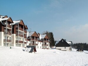 Een besneeuwde skiresort met meerlaags gebouwen, waaronder een hotel met balkons en een skilift is zichtbaar op de achtergrond.