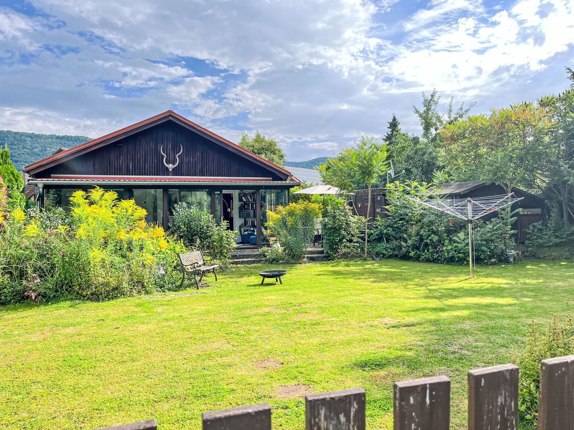 A rustic cabin with a porch, surrounded by lush greenery and a clear sky.
