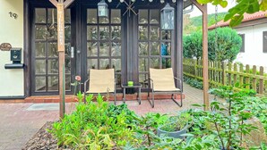 Un rincón exterior acogedor con dos sillas y una mesa, rodeado de abundante vegetación y una valla de madera.