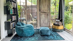 Un rincón acogedor para leer con una estantería grande, un sillón de peluche color turquesa y un reposapiés a juego, todo frente a un amplio ventanal con vistas a un jardín.