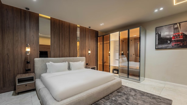 A modern bedroom with a large bed, wooden panel walls, a glass wardrobe, and a framed picture of a double-decker bus. - George Residence Thompson Ave Ikoyi (Lagos)