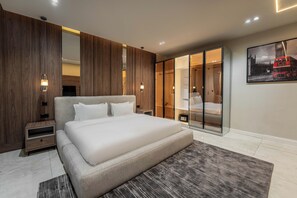 A modern bedroom with a large bed, wooden panel walls, a glass wardrobe, and a framed picture of a double-decker bus. - George Residence Thompson Ave Ikoyi (Lagos)
