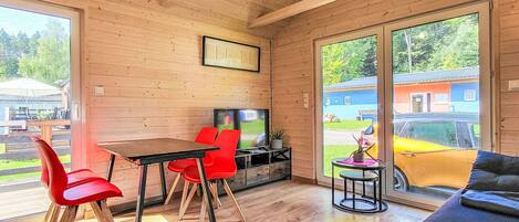 A modern interior with wooden walls, a dining area with red chairs, a sofa, and a TV.