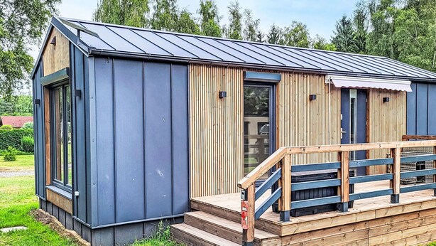 Eine kleine, moderne Holzhütte mit einer Holzterrasse und einem Metalldach.