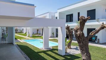 Un bâtiment moderne doté d’une piscine, de colonnes blanches et d’un arbre.