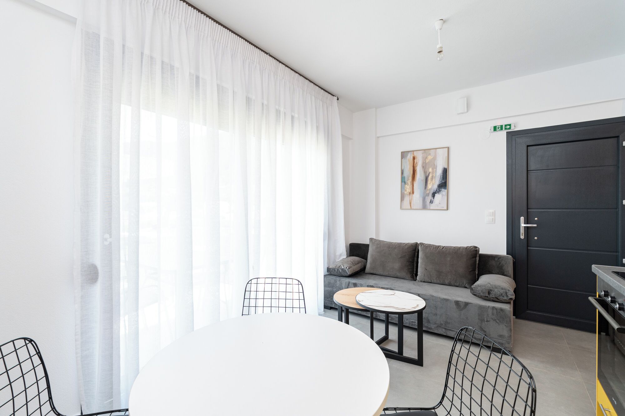 Un salon moderne avec un canapé, une table à manger et des chaises. Il y a un tableau au mur et une porte avec un panneau indiquant la sortie.