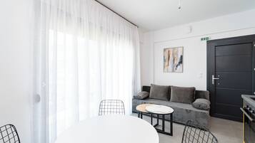 Un salon moderne avec un canapé, une table à manger et des chaises. Il y a un tableau au mur et une porte avec un panneau indiquant la sortie.