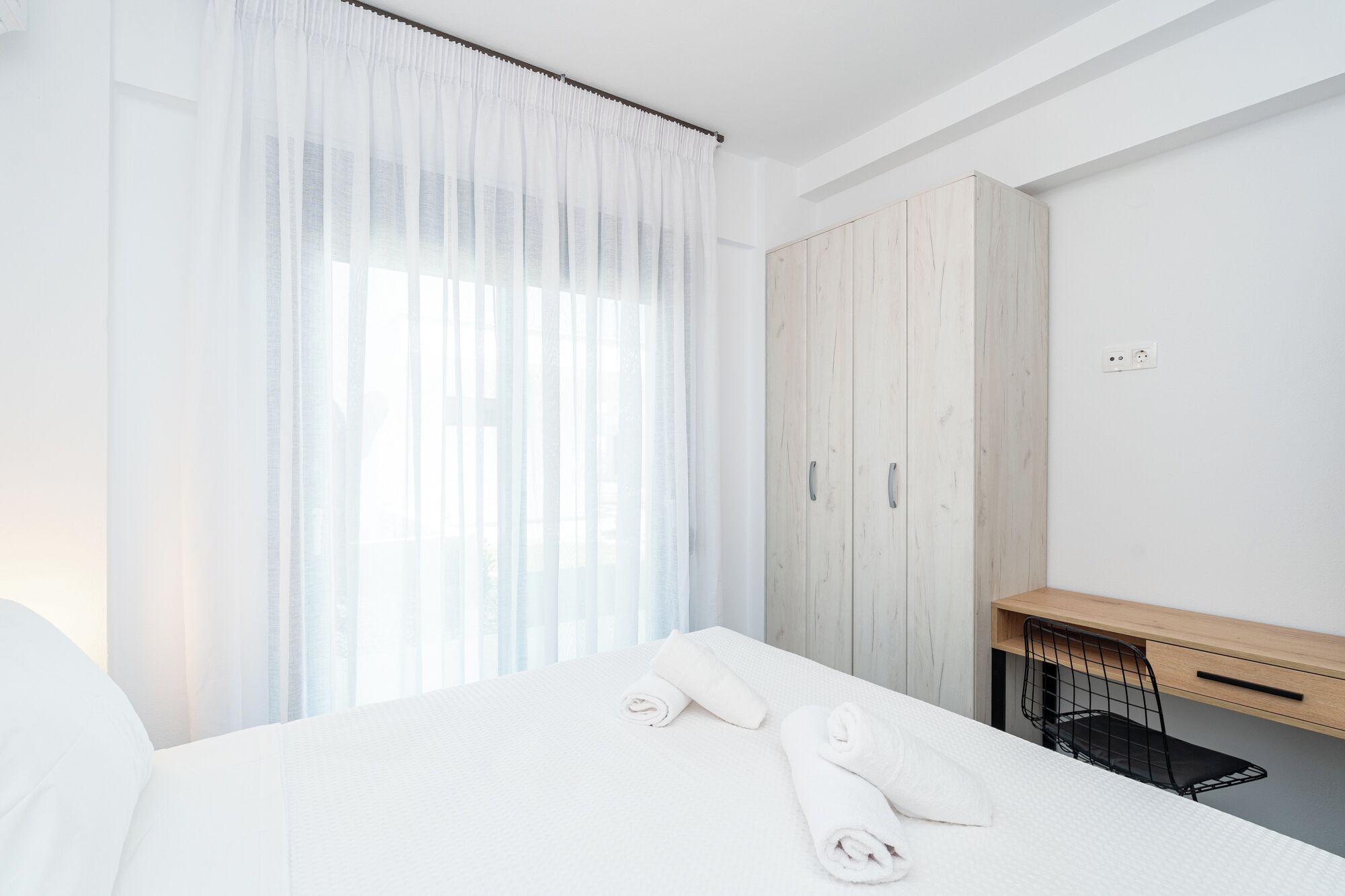 Hotellihuone, jossa on sänky, puinen vaatekaappi, työpöytä ja tuoli.