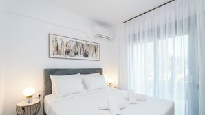 A hotel room with a large bed, white bedding, a framed abstract painting, an air conditioning unit, and sheer curtains. - White Dream One-bedroom Apartment With Pool Access (Thasos)