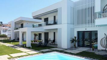 Un immeuble résidentiel moderne à plusieurs étages, doté d’une piscine, d’un espace extérieur aménagé et offrant une vue sur un ciel dégagé.