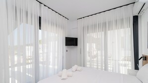 A modern hotel room with a large bed, white curtains, and a flat-screen TV mounted on the wall. - Emerald Three-Bedroom Villa with Private Pool and Rooftop (Kavala)