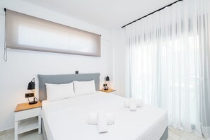 A modern hotel room with a large bed, two bedside tables with lamps, a window with sheer curtains, and a wall-mounted light fixture. - Emerald Three-Bedroom Villa with Private Pool and Rooftop (Kavala)