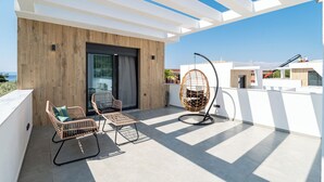 A modern outdoor patio with wicker furniture, a hanging chair, and a view of the sea. - Emerald Three-Bedroom Villa with Private Pool and Rooftop (Kavala)