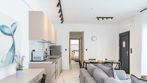 A modern kitchen with a microwave, stove, and sink. There is a dining area with a table and chairs, and a living room with a sofa. - Emerald Three-Bedroom Villa with Private Pool and Rooftop (Kavala)
