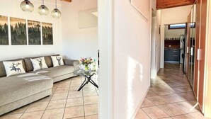 Sala de estar con sofá, una mesa de centro y decoración en la pared. Se ve un pasillo que conduce a una zona de cocina.