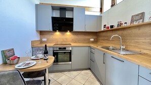 Cocina compacta con encimera de madera, electrodomésticos de acero inoxidable y comedor con mesa para dos.