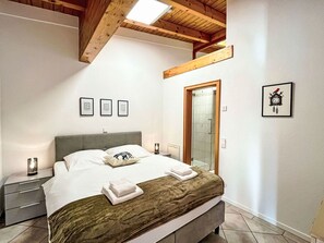 Un dormitorio moderno con cama, mesitas de noche, techo de madera y una puerta.