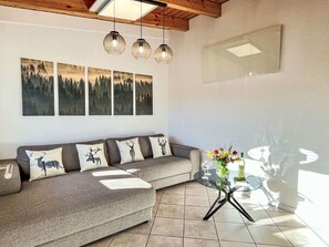 Una sala de estar con un sofá gris, cuatro cuadros colgados en la pared y una mesa de centro de vidrio con un arreglo floral.